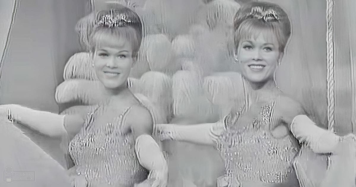 Two young adult female performers in matching silver sequined dresses, likely mid-20th century style, standing against a curtain backdrop with a plush chair behind them.