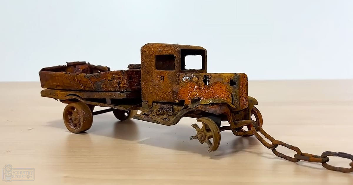 Rusted toy truck with chain, weathered appearance, indoors on light wooden surface against plain white wall.