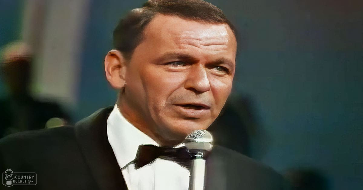 A middle-aged man wearing a formal tuxedo stands on what appears to be a stage or performance area with soft, warm lighting.