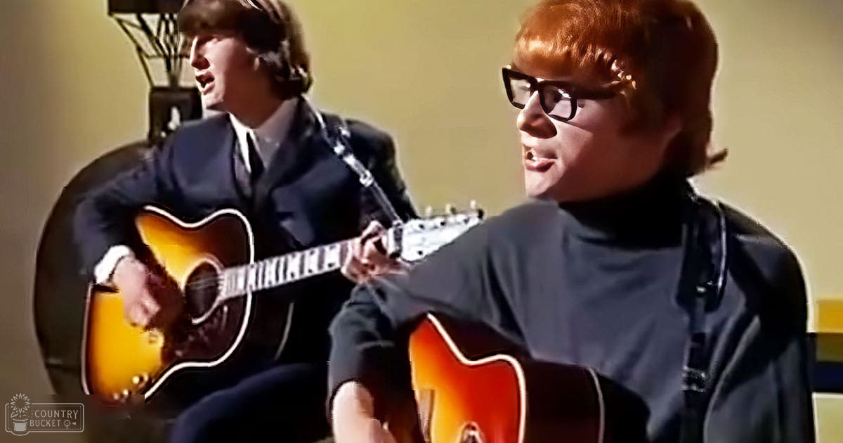 A musical performance scene with two young adult males in formal and semi-formal attire, set indoors under warm lighting.