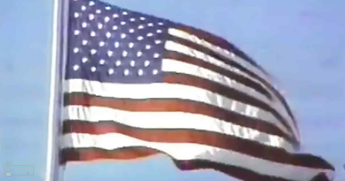 American flag attached to a pole against a clear blue sky, suggesting an outdoor event or park setting with natural daylight and no specific season indicated.