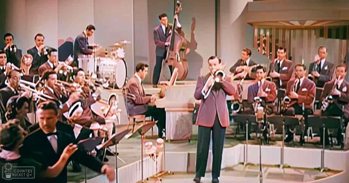 A musical performance scene with brass and stringed instrument players on a brightly lit stage in an indoor venue.