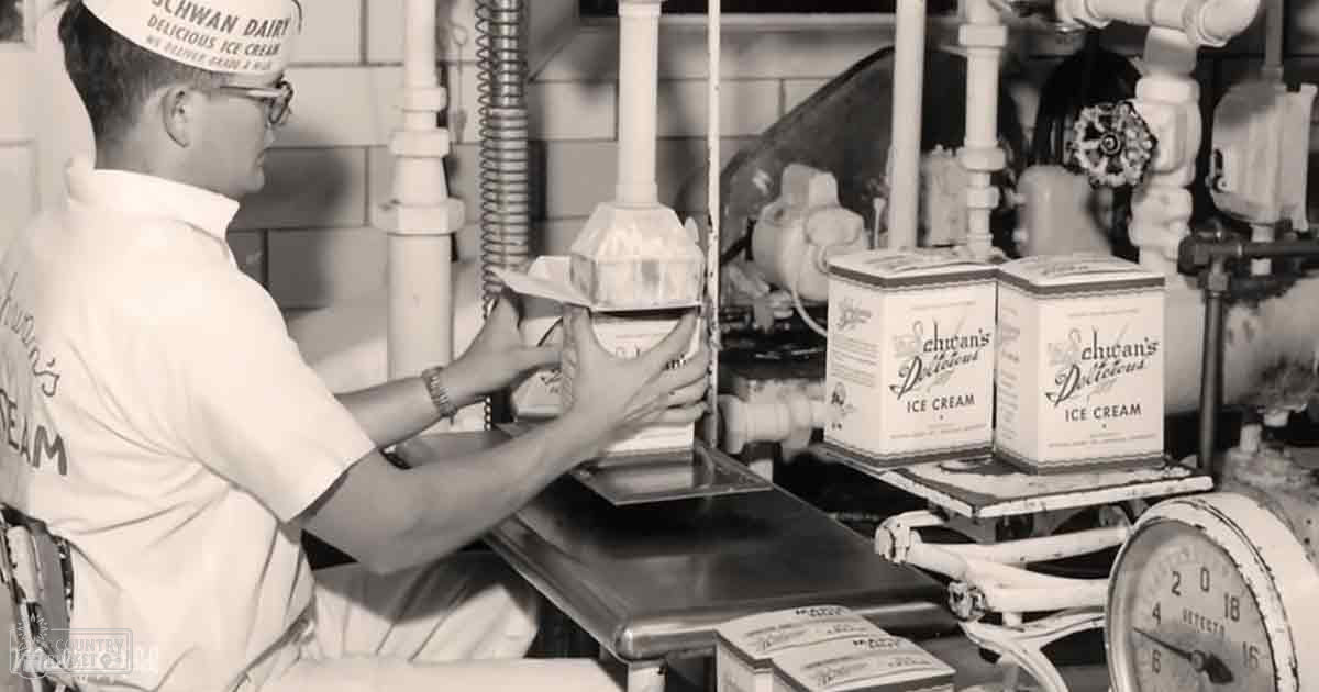 An adult male worker from mid-20th century America wearing a 'Schwan Dairy' uniform, standing at an ice cream production line with visible branded items and machinery.