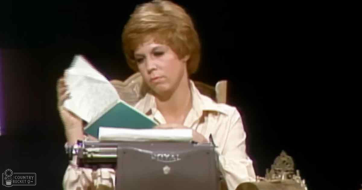 A young adult female wearing a light-colored, mid-20th-century button-up shirt is positioned in front of a vintage Royal typewriter and dark backdrop in an indoor setting.