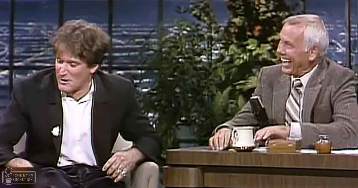 A middle-aged man wearing a dark suit jacket over a white shirt with a light-colored tie stands next to an older adult male in a studio setting, both dressed formally for what appears to be a television talk show.