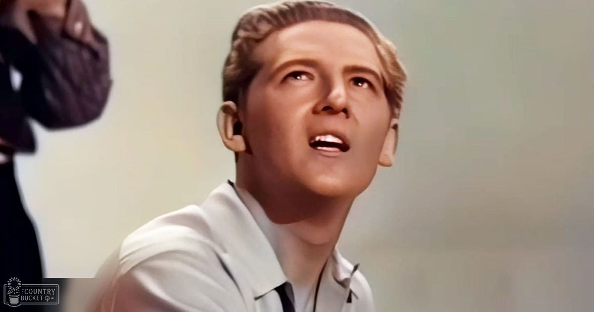 A young adult male in a light-colored collared shirt with a tie stands indoors against a simple wall under soft lighting.