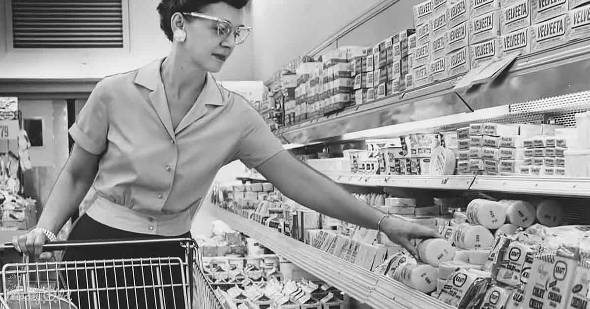An adult female wearing a mid-20th century-style button-down blouse with dark pants or skirt shopping in a grocery store, holding a shopping cart filled with dairy products.