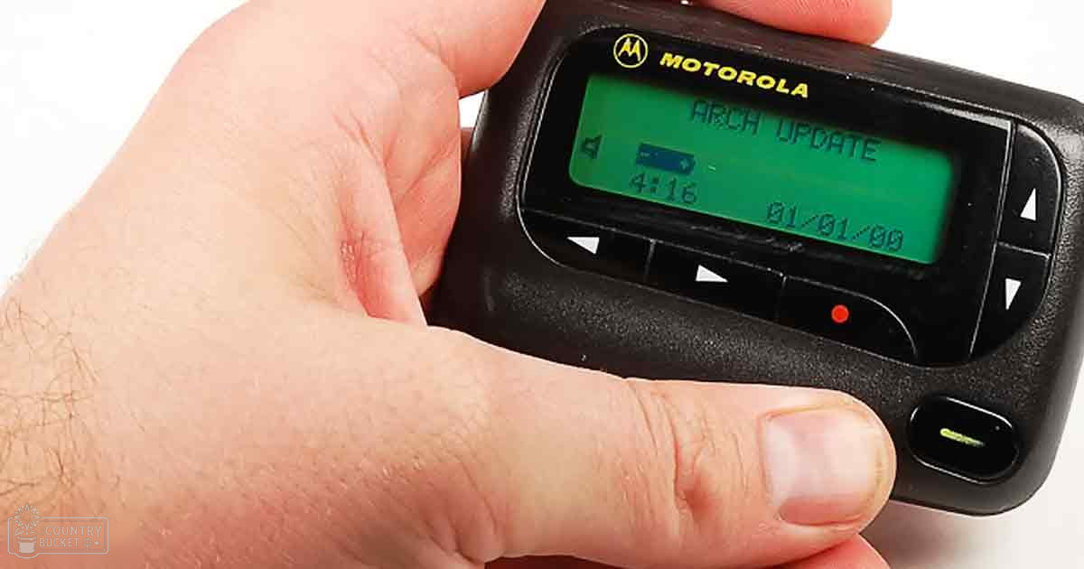 A hand holding a Motorola pager displaying 'ARCH UPDATE' against a plain white background in an indoor studio setting