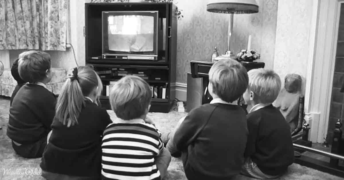 A group of children watching television in a living room with wallpapered walls, suggesting it's likely winter or spring.