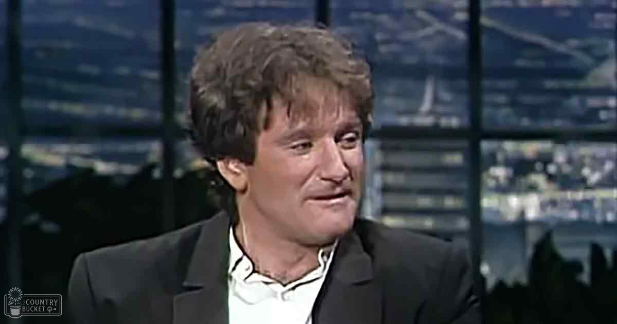 Middle-aged adult male wearing dark blazer, white shirt, and black tie in an indoor studio with cityscape backdrop at night.