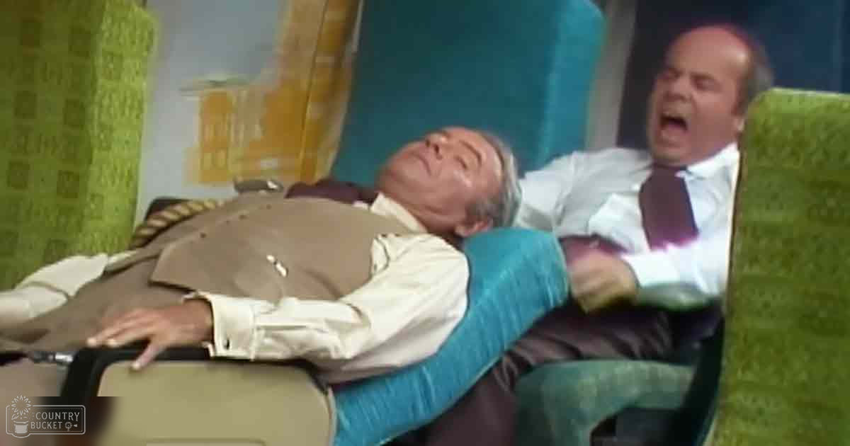 Two middle-aged men in a vintage airplane cabin, wearing formal attire and engaging in a humorous interaction.