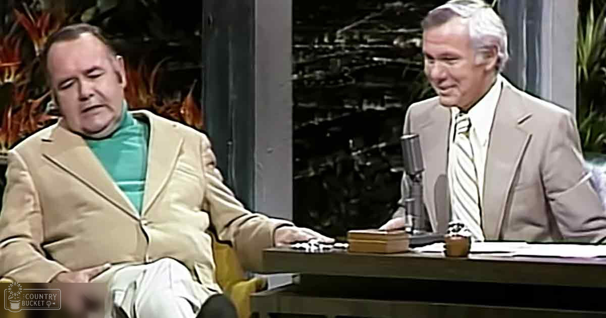 Two middle-aged to older adult males in formal attire seated at a desk with stage lighting and decor typical of mid-20th century talk show sets.
