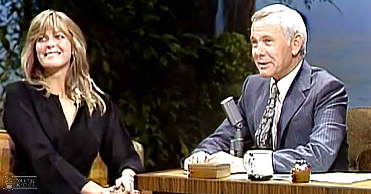 Two individuals seated at a talk show set with foliage in the background, suggesting an indoor studio designed to mimic outdoor scenery.