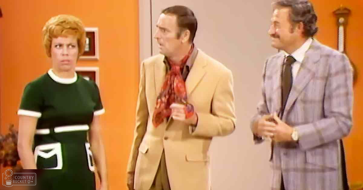 A mid-20th century indoor scene with three adults dressed formally and vintage-style, set against orange walls with home decor elements like a wall clock and bookshelf in what appears to be a living room or office.
