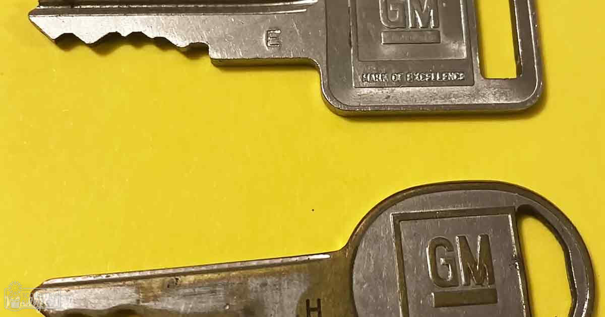Two GM car keys with 'Mark of Excellence' text displayed against a bright yellow background.