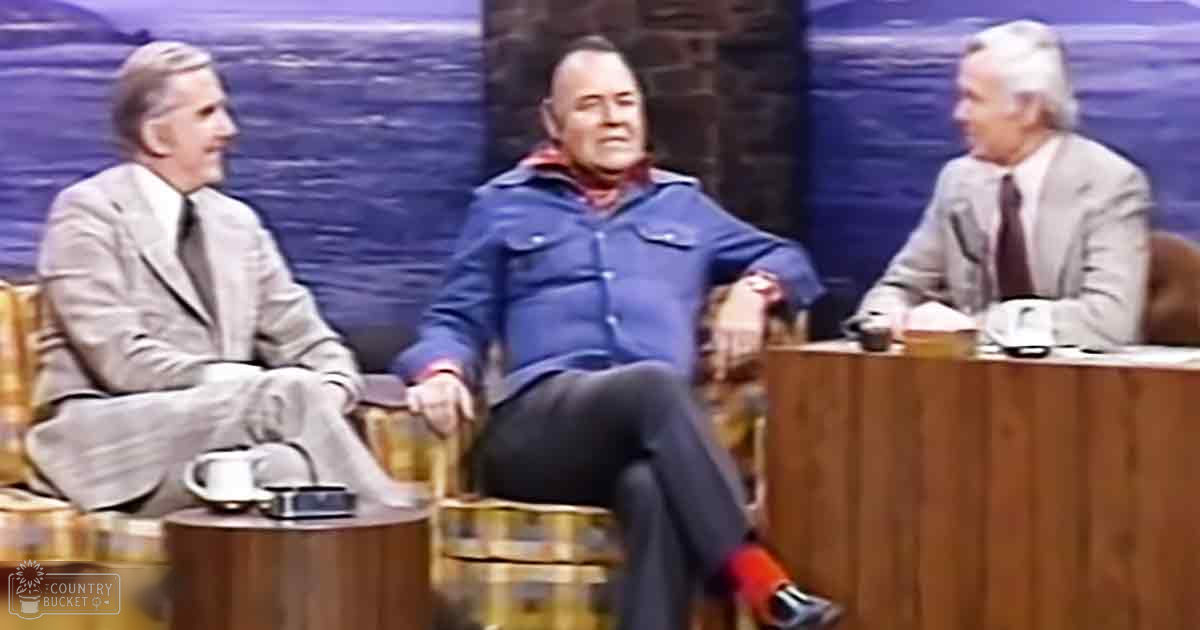 Three older adult men in a talk show set with blue-toned water imagery as background, suggesting an ocean view. Bright indoor lighting typical of television production settings.