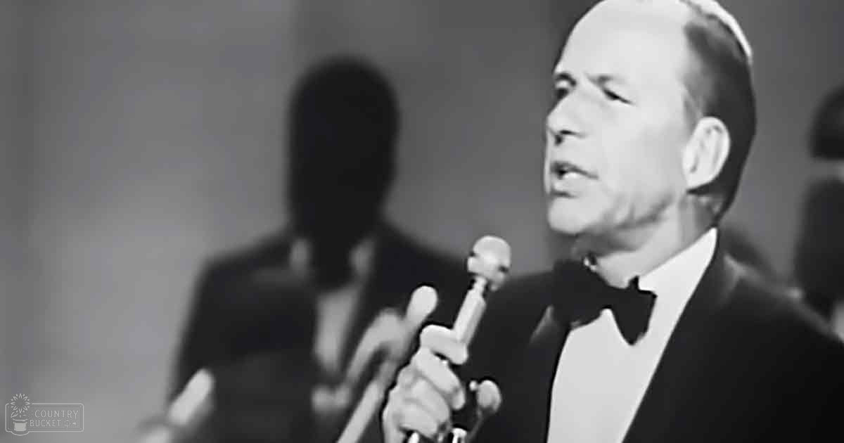 A man singing into a microphone with a tuxedo in a performance setting from the mid-20th century.