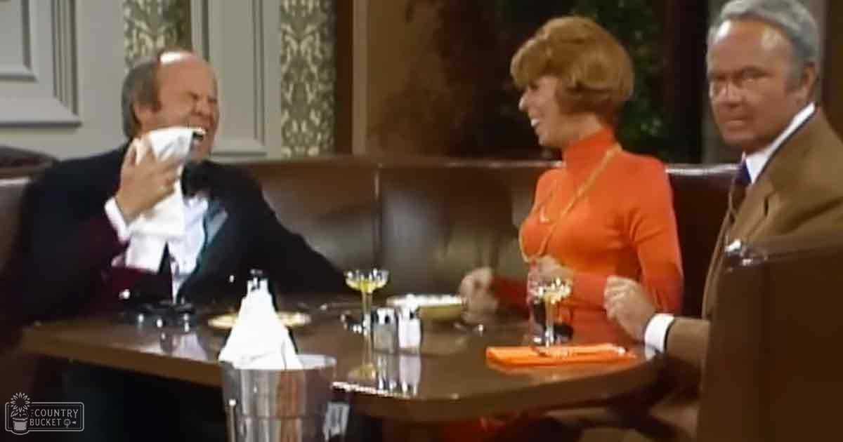 A restaurant scene with an adult male holding a napkin near his mouth, surrounded by two other individuals seated at a booth table with dark leather seating and wooden tables. The background suggests an elegant indoor dining area with decorative floral patterns.