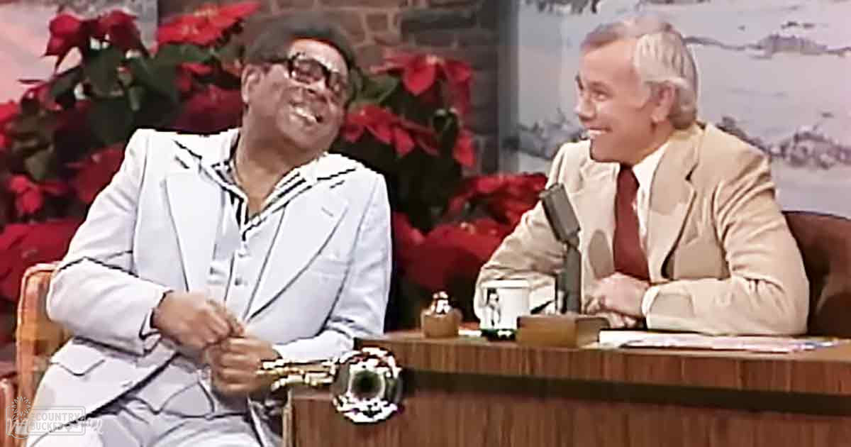 Talk show host and guest in studio setting with festive poinsettias, bright lighting, and holiday-themed decor.