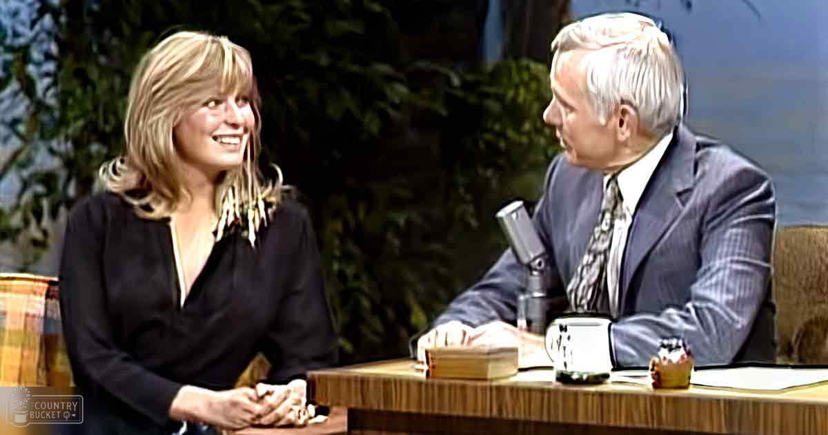 Two adults seated at a table with muted tones and indoor greenery, suggesting a controlled studio environment for an interview or talk show.