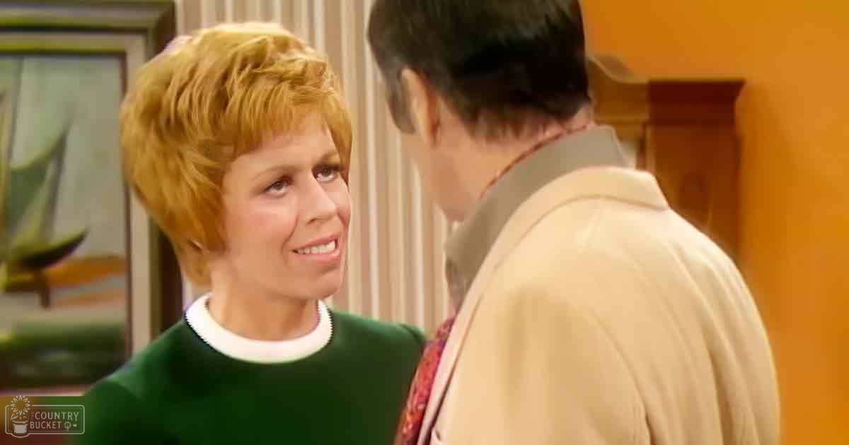Adult female in relaxed fit sweater with crew neck collar trim and long sleeves, standing indoors near a green sofa and framed artwork with vertical stripes.