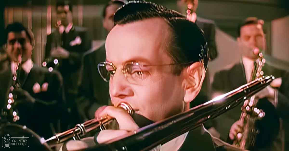 Young adult male playing a trombone in an indoor jazz club setting with dim lighting, surrounded by other adults in dark suits.