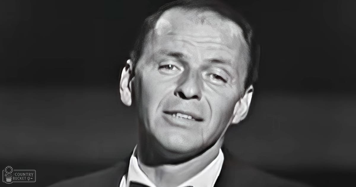 Middle-aged adult male wearing a tailored formal suit jacket with a white collared shirt, set against an indoor backdrop illuminated by focused studio lighting.