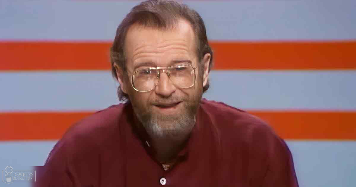 An older adult male in a studio setting with a maroon button-up shirt, simple orange and white striped backdrop