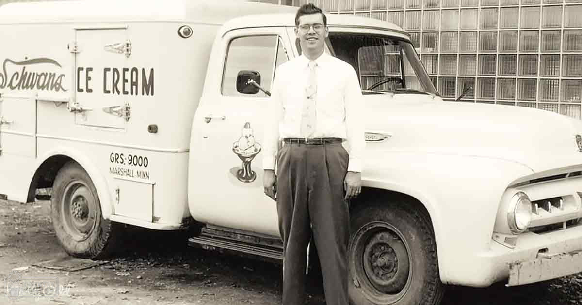 A young adult male wearing a white dress shirt, dark trousers, and glasses stands next to an ice cream delivery truck labeled 'Schwan's Ice Cream' in Marshall, Minnesota.