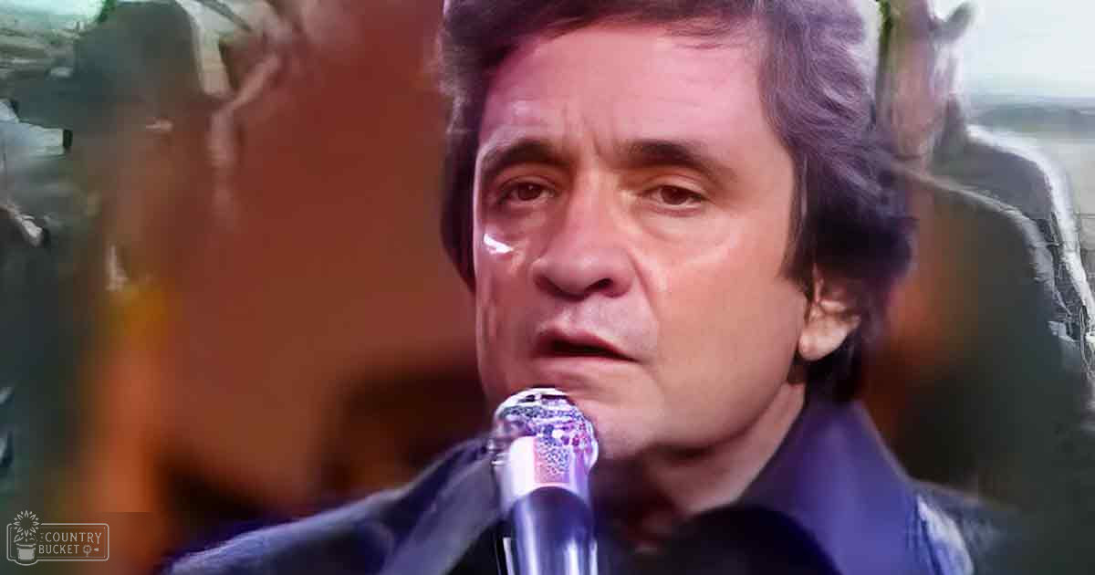 A middle-aged man in a dark-colored suit jacket stands on stage, holding a microphone against his mouth.
