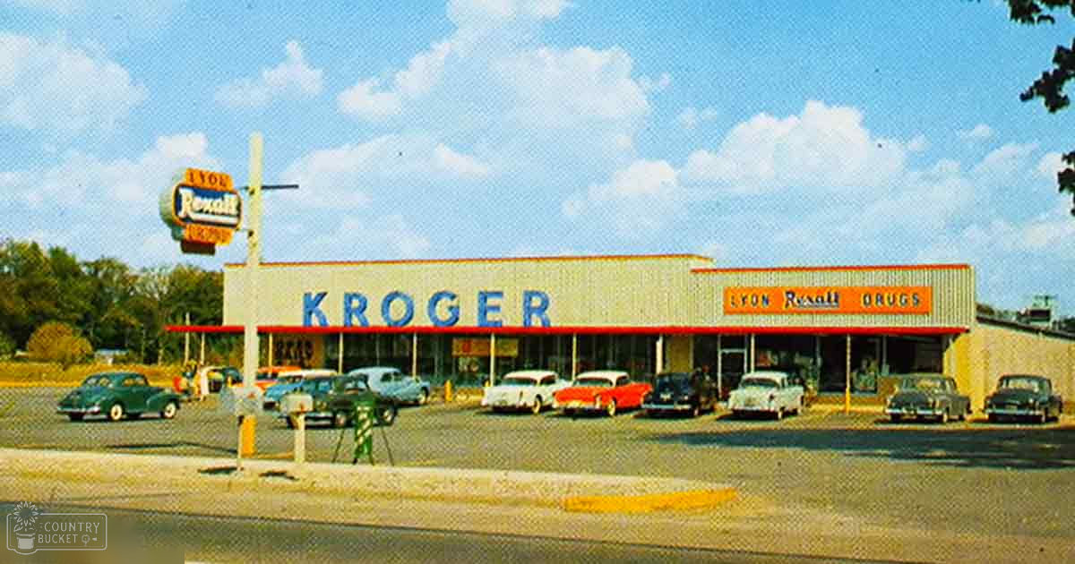 Vintage cars parked outside Kroger grocery store with 'Lyon Rexall Drugs' gas station sign visible, daytime scene with greenery and clear sky, spring or summer setting.