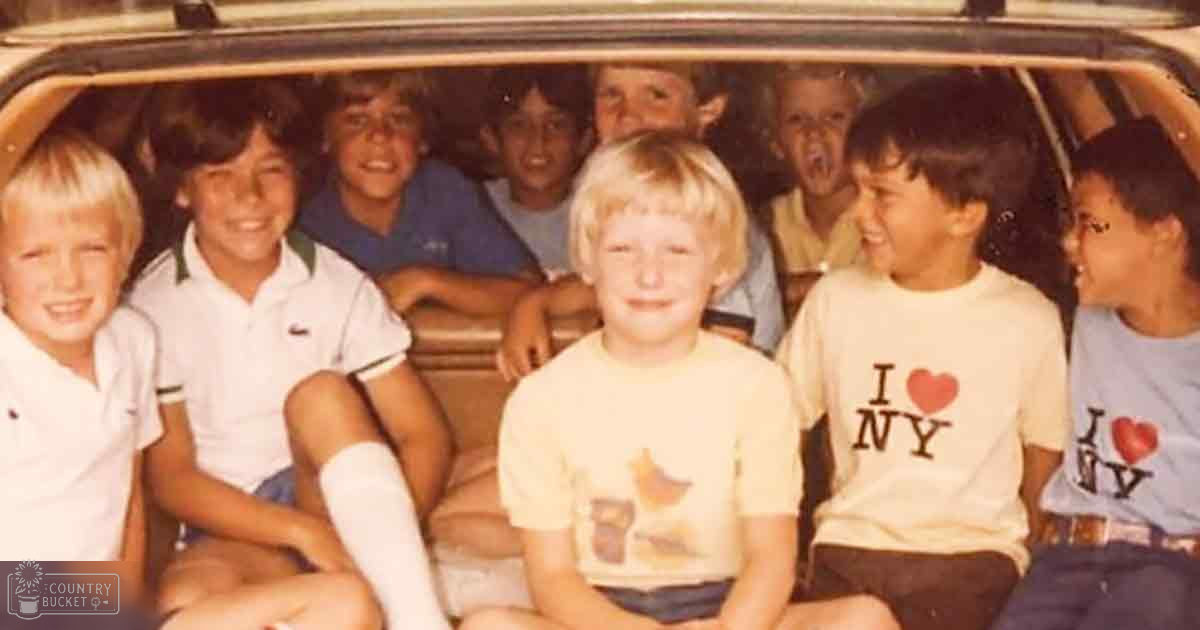 A group of children wearing casual summer attire sit inside a vehicle under natural daylight.
