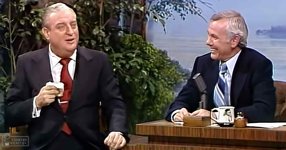 Two older adults in a talk show setting with wooden furniture and indoor plants.