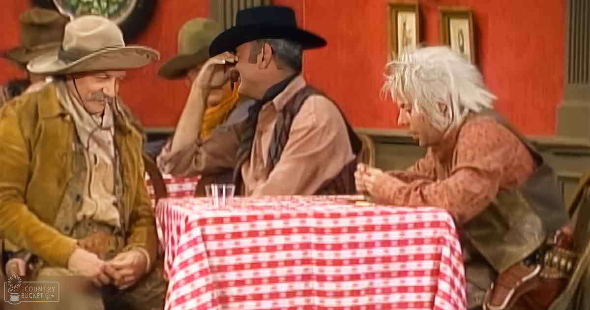 Three older adult males in a Western-themed saloon setting, wearing cowboy hats and holding small items; wooden paneling with framed artwork, red-and-white checkered tablecloth.