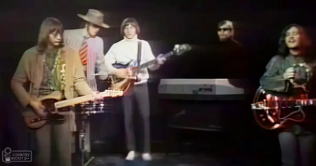 A musical performance scene from the late 1960s to early 1970s, with young and adult male musicians in period-appropriate attire on a dimly lit stage.
