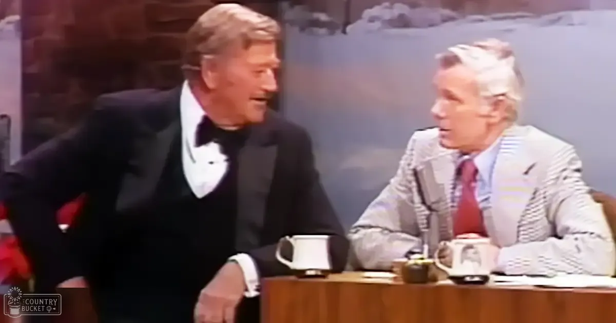 Two adults in a studio setting with a mid-20th century style, surrounded by talk show furniture against a painted natural backdrop.