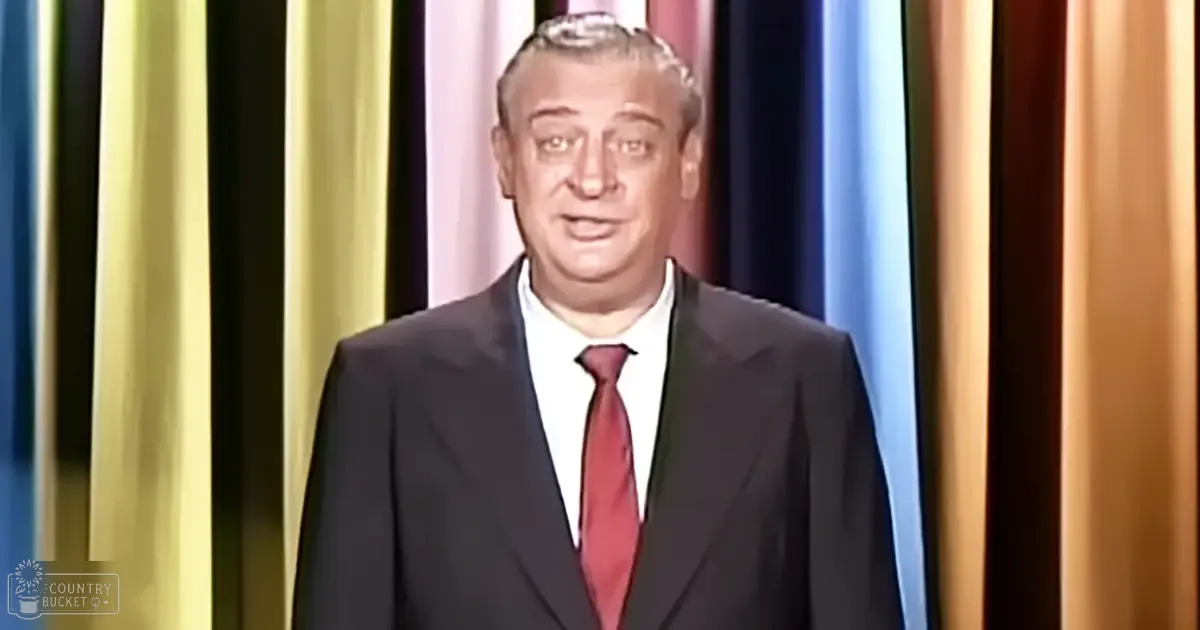 Middle-aged man wearing a dark tailored suit with a white dress shirt and red tie in an indoor studio setting with vertically striped curtains as backdrop.