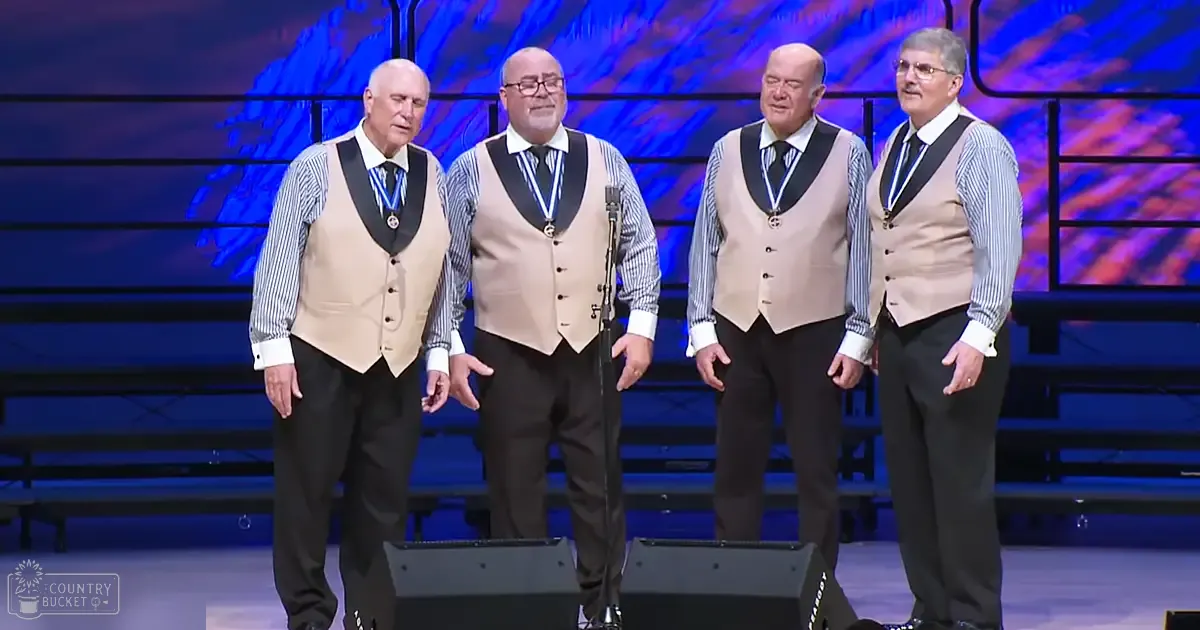 A barbershop quartet performing on stage with abstract blue and purple backdrop under artificial lighting.