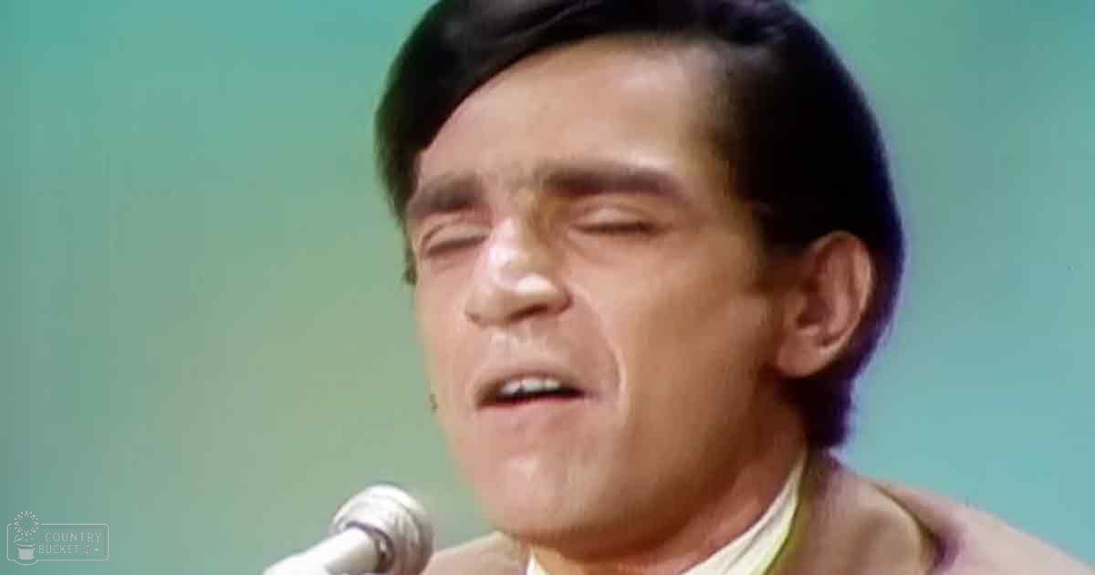 A middle-aged adult male singing into a microphone in an indoor studio setting.