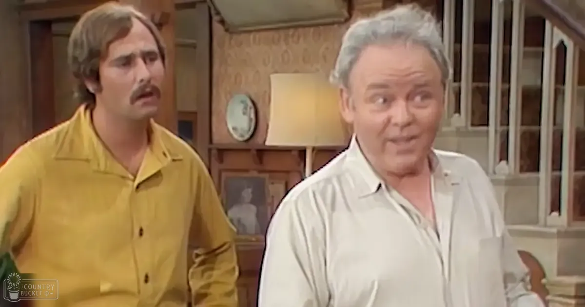 Two adult males in a domestic setting with wooden paneling and wallpaper with a subtle pattern; one wearing a yellow button-up shirt from the mid-20th century, another in a light-colored shirt.