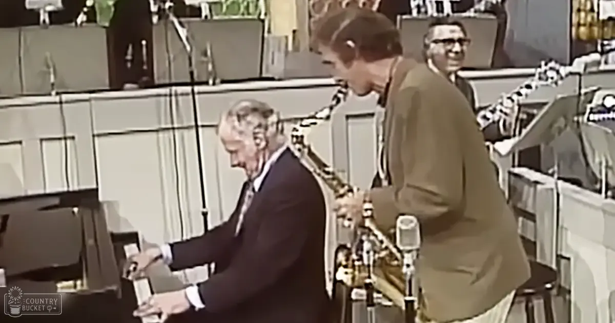 A mid-20th-century indoor setting with an older adult male singer seated and another adult male standing, both dressed formally; a piano is partially visible on the left with microphones positioned for performance recording.