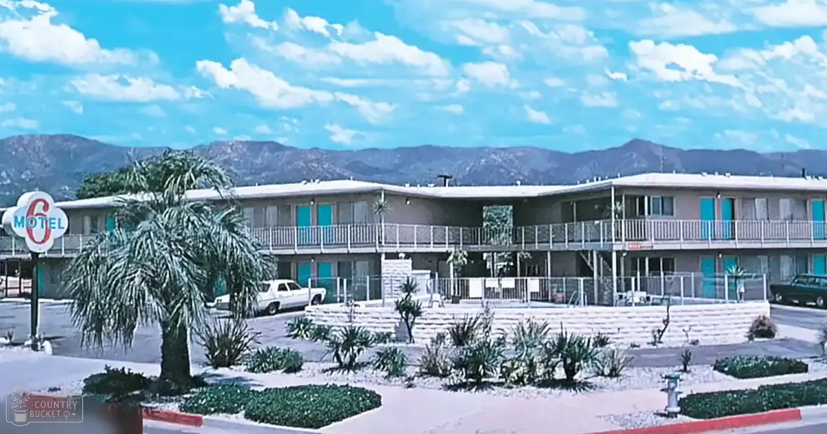 Motels sign and landscaping with palm trees, bushes, and a white pickup truck under clear skies with mountains in the background during midday spring or summer.
