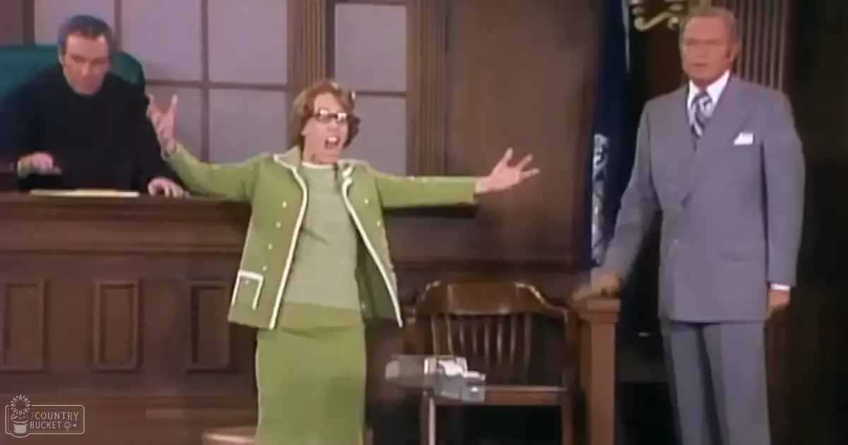 Adult female wearing a green 1970s-style dress suit with white trim, seated at a wooden bench in a courtroom setting.
