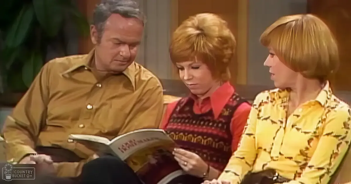 An adult male singer reading from a book, flanked by two women seated beside him in what appears to be a mid-20th-century living room with wooden paneling and natural or soft indoor lighting.