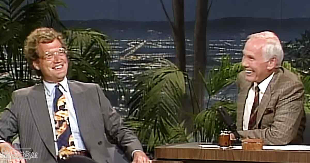 A talk show set with palm trees in a nighttime cityscape backdrop, suggesting an outdoor filming location.