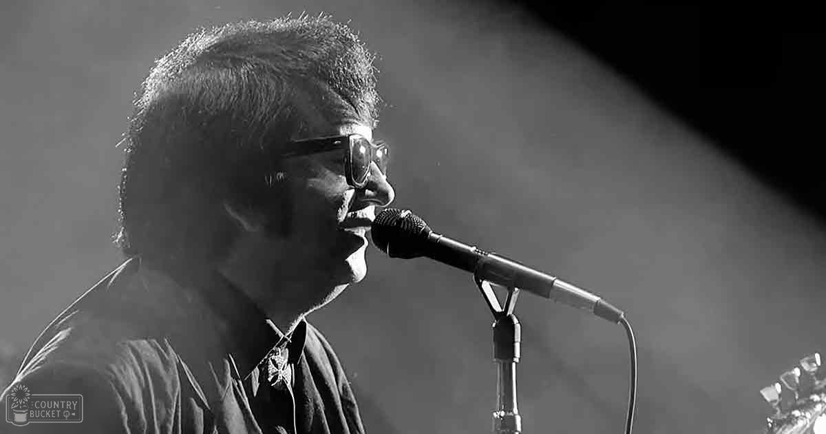A middle-aged male singer performing at an indoor music venue with a spotlight on him.