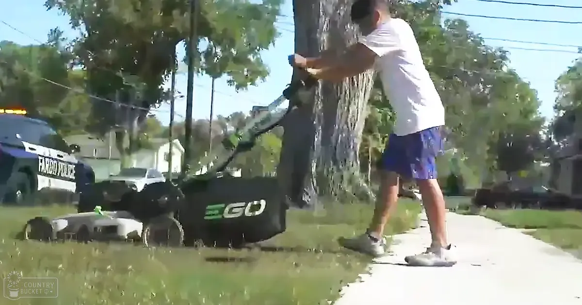 An adult male mowing grass with an EGO lawnmower in a suburban neighborhood during the daytime under clear and sunny weather.