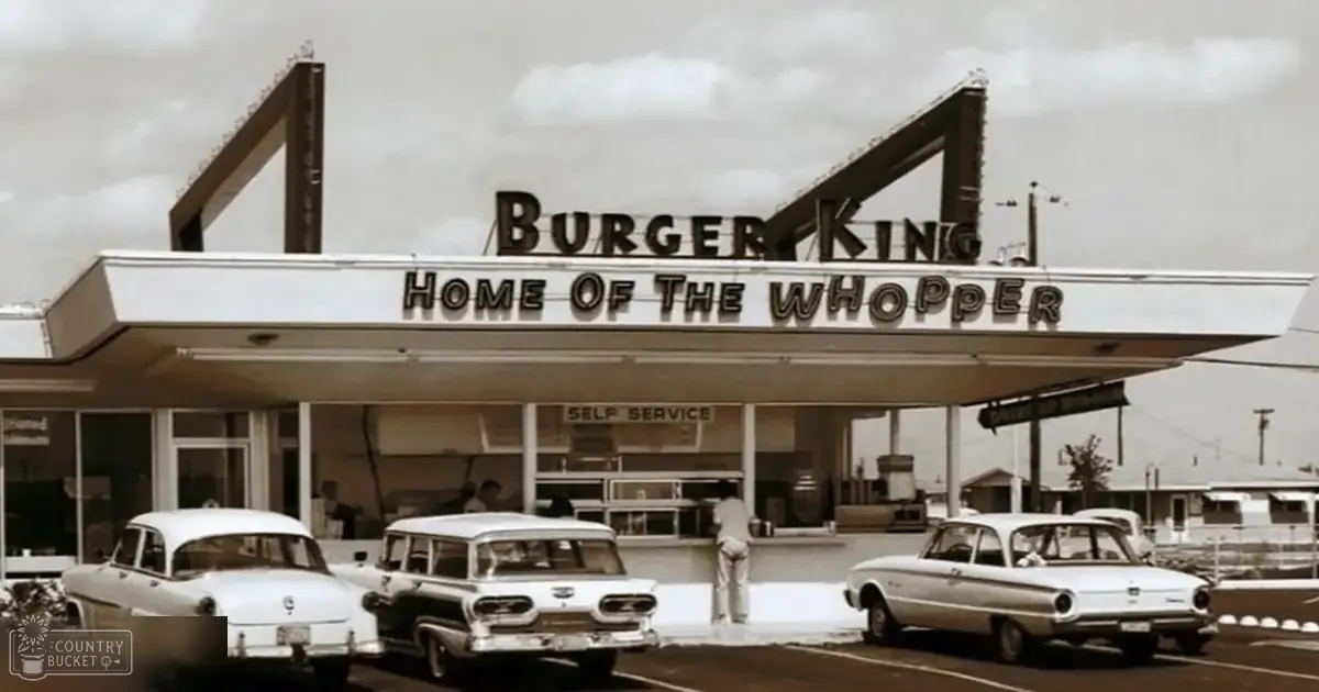 An urban Burger King restaurant setting with vintage cars parked in front during daytime.