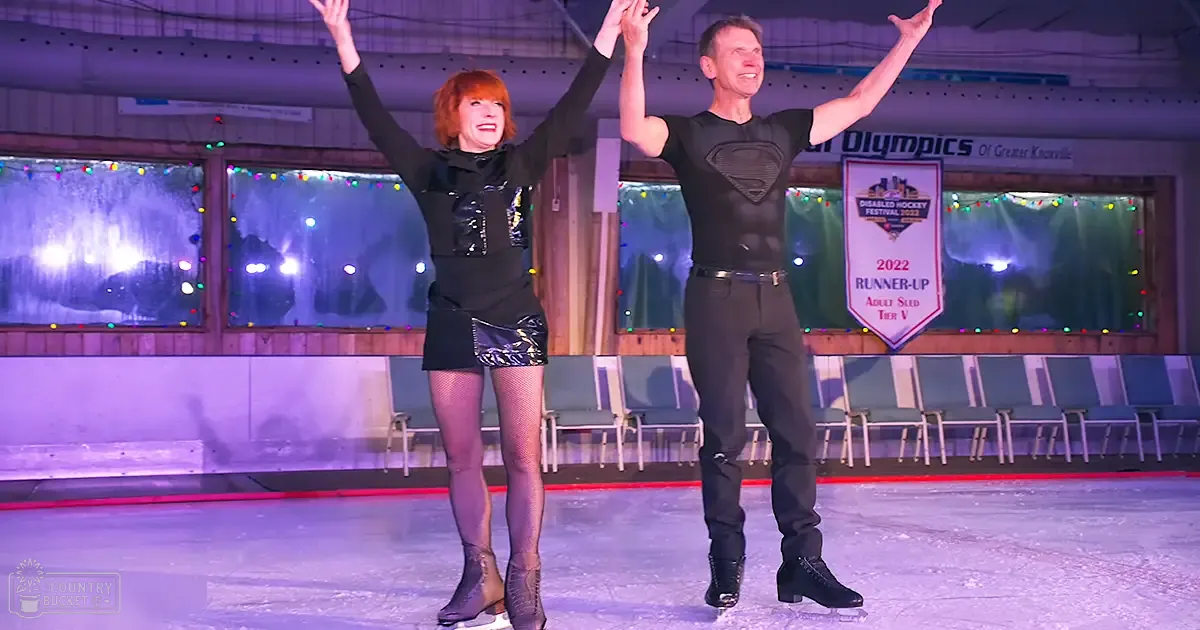Adult couple skating together at an indoor ice rink in Greater Knoxville, wearing black outfits with textured patterns and accessorizing with fishnet stockings and a belt.
