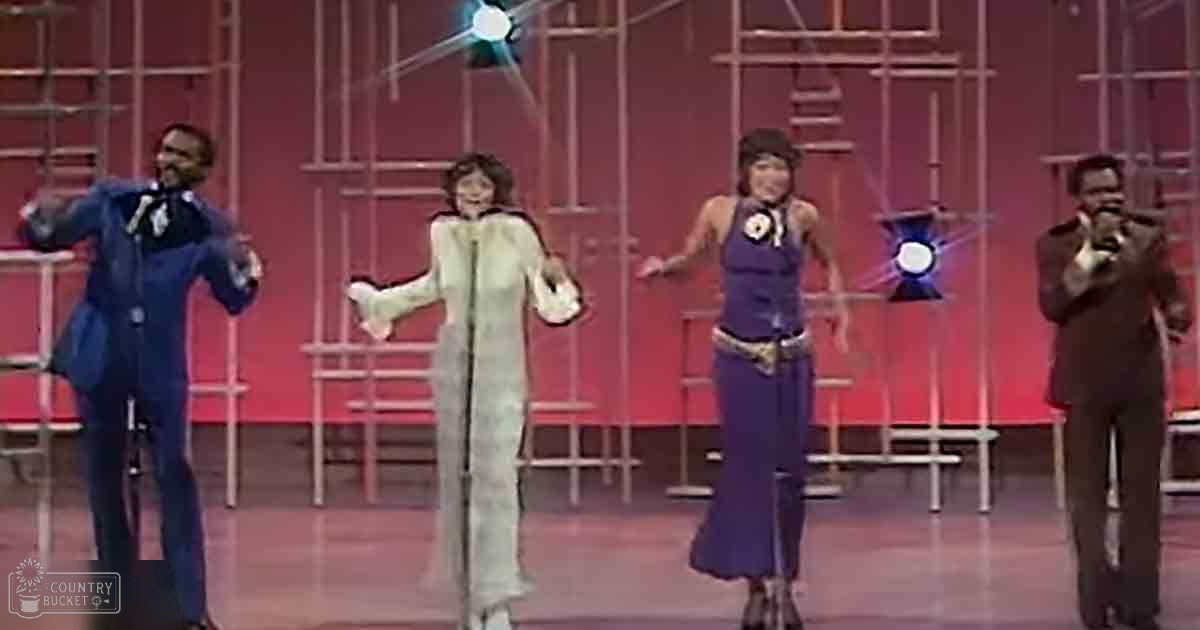 A performance scene with performers on a stage with geometric patterns against a red backdrop, mid-20th century style attire.